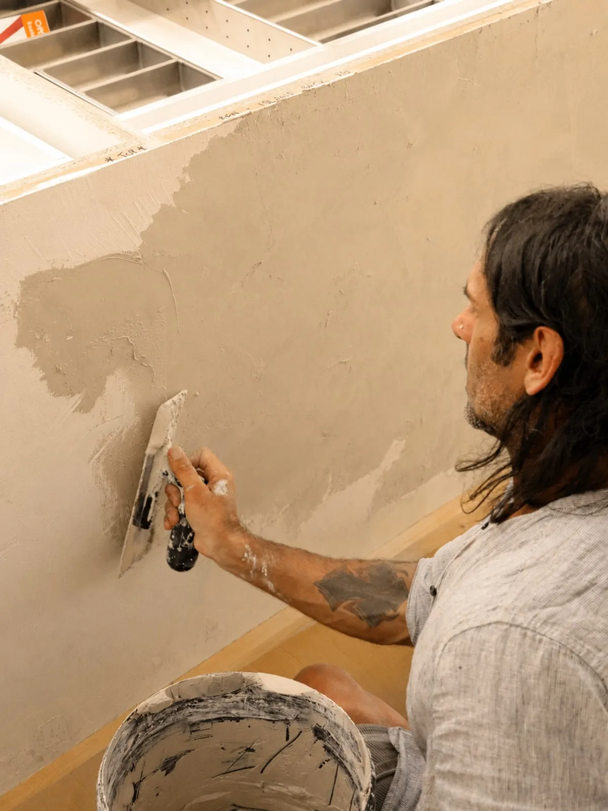 Francis kneeling, hand-applying microcement with a float